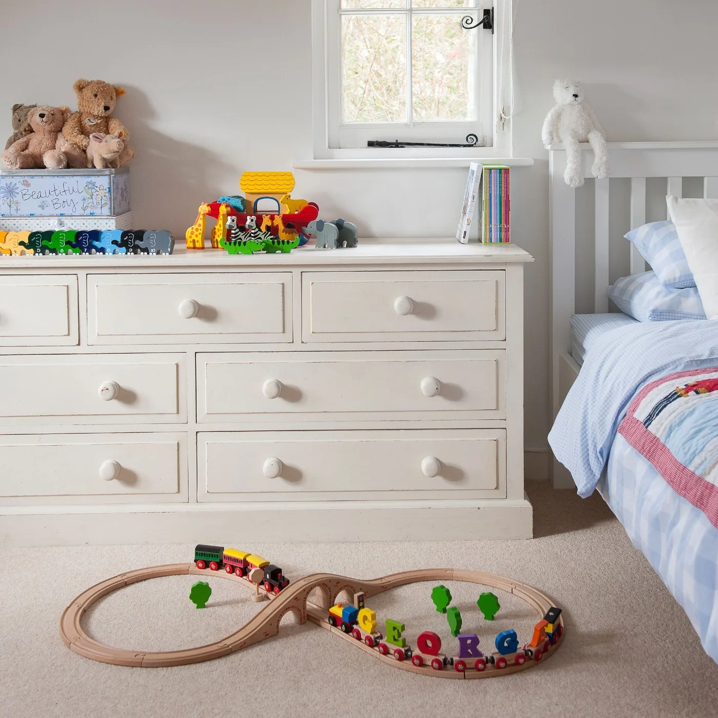 Wide white dresser displaying a toy ark, animal figures, books and soft toys beside a bed
