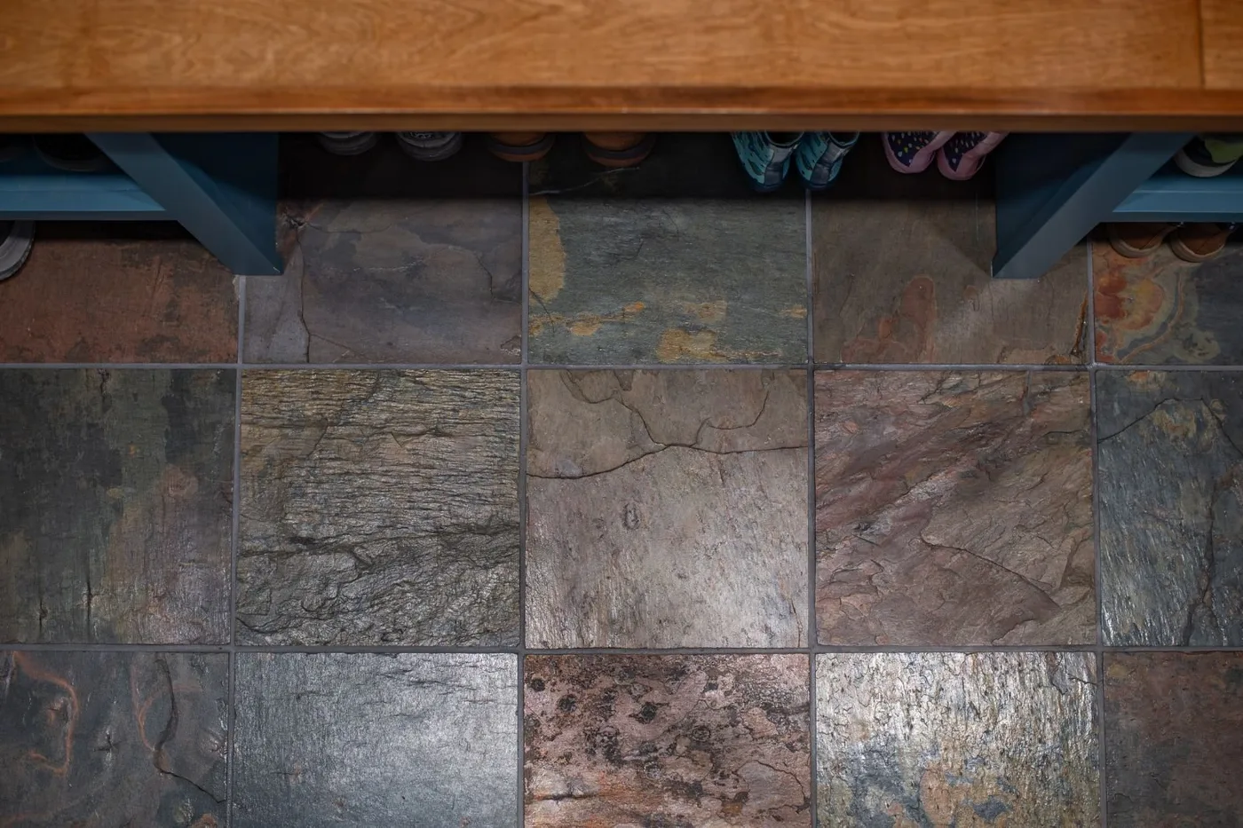 Multicolored textured floor tiles below a wooden mudroom bench and blue shoe compartments.