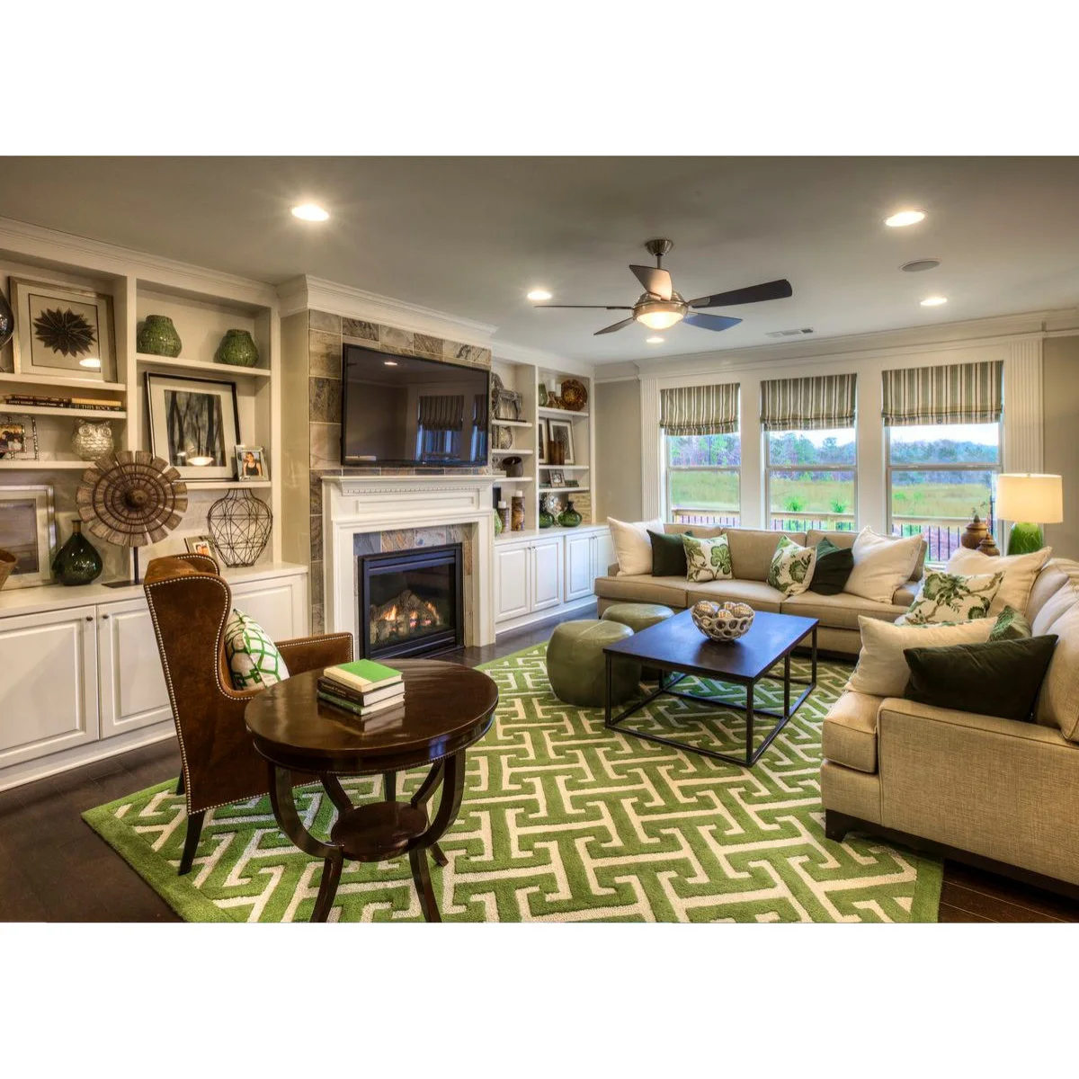 Pale seating surrounds a rectangular coffee table on a green rug, with a round table and brown chair at the near end.