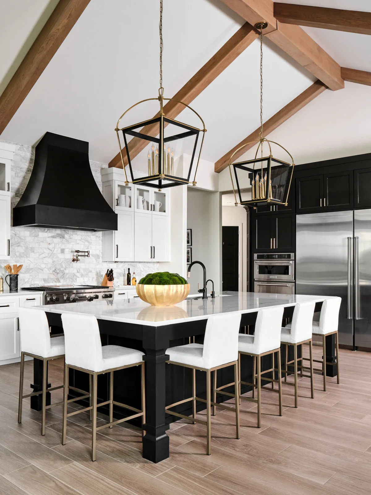 A black island sits beneath exposed beams with a row of white-backed stools.