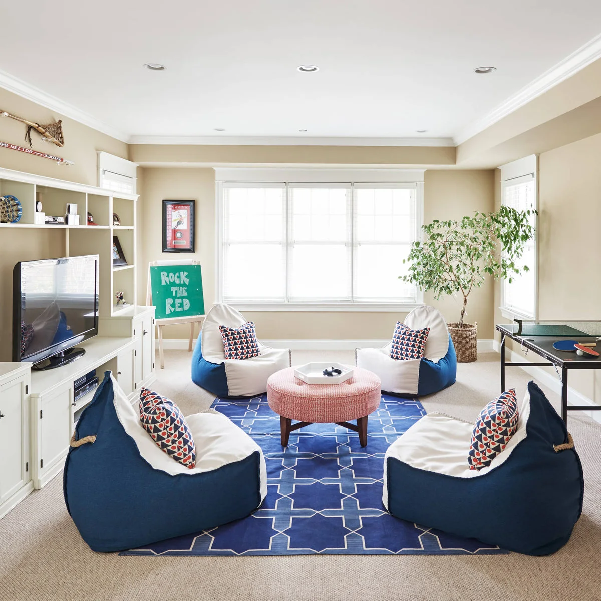A blue-and-white media room with a television, low cabinets, blue beanbag seats and a tray of game controllers.