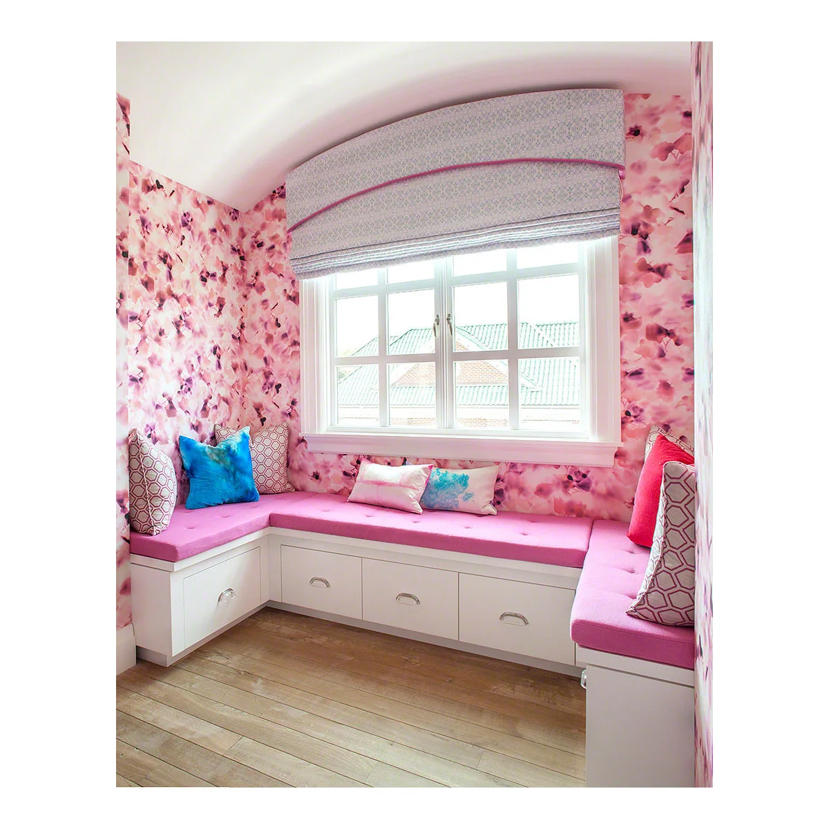 White window-seat drawers with pink cushions, floral walls and a curved-top blind