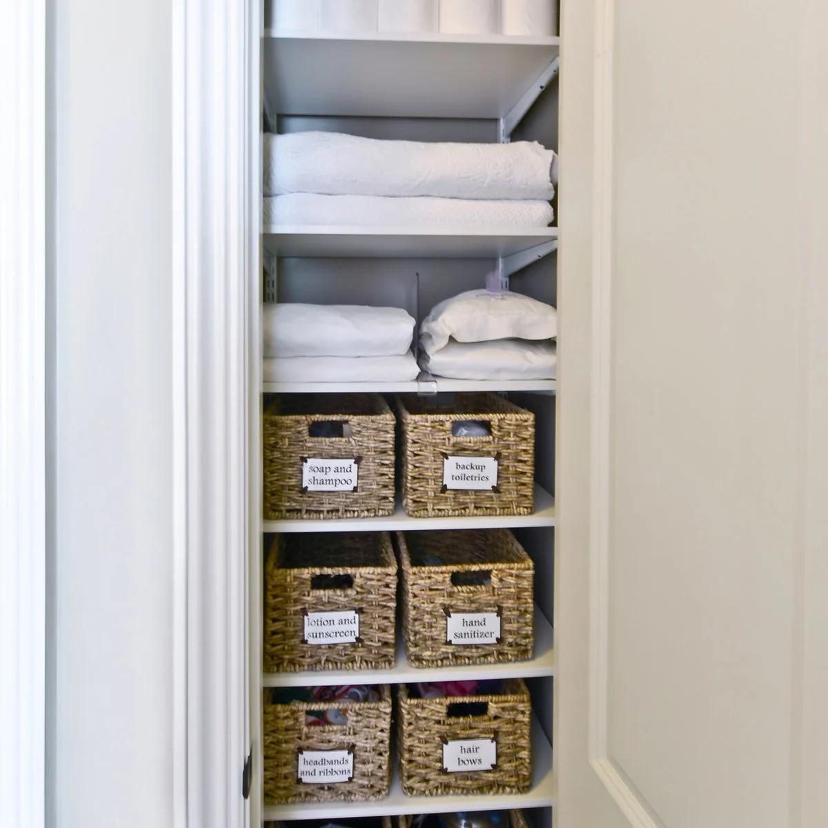 Narrow linen cupboard with folded towels and labeled woven baskets