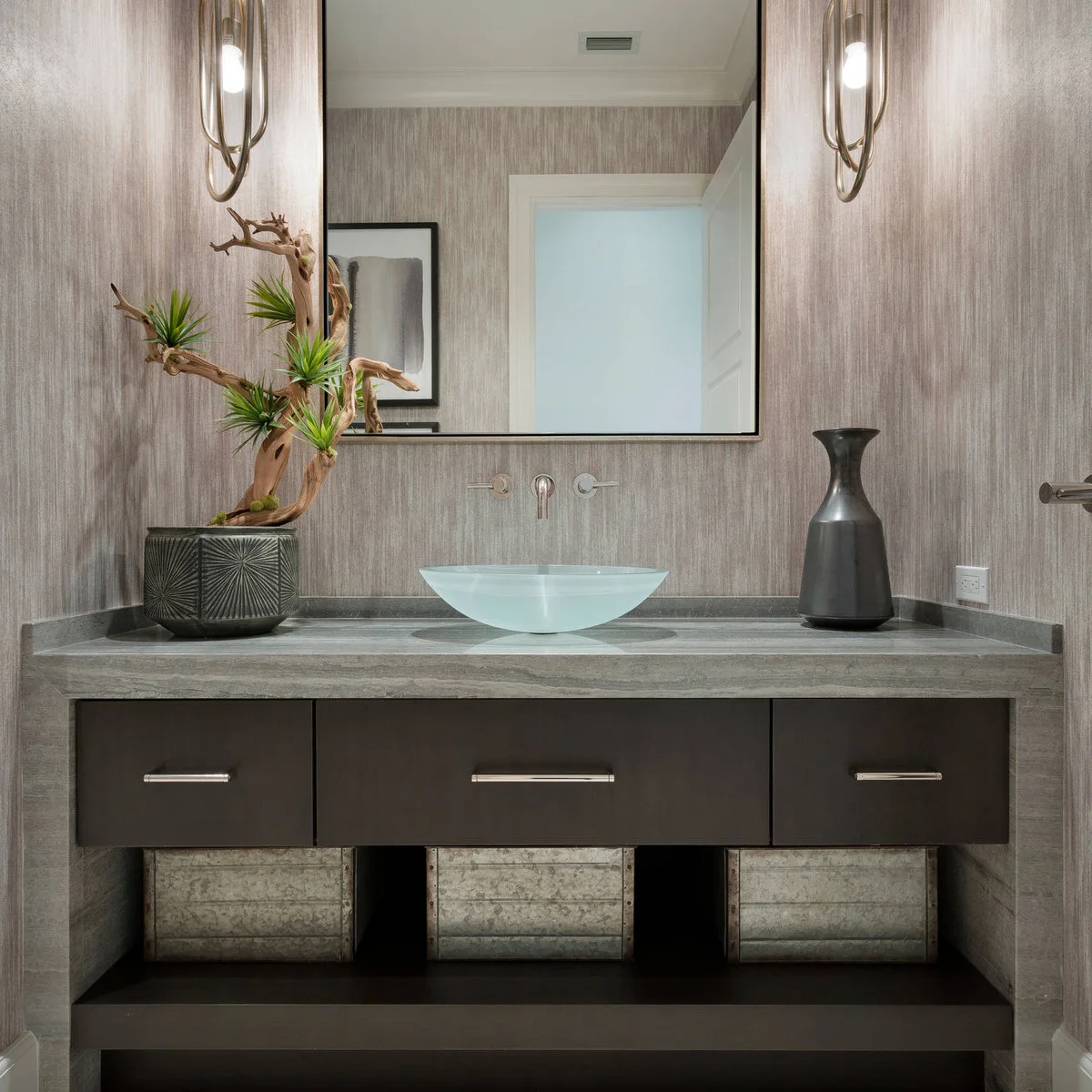 A pale aqua vessel bowl sits on a wide gray counter above dark drawers and an open shelf with three storage boxes.