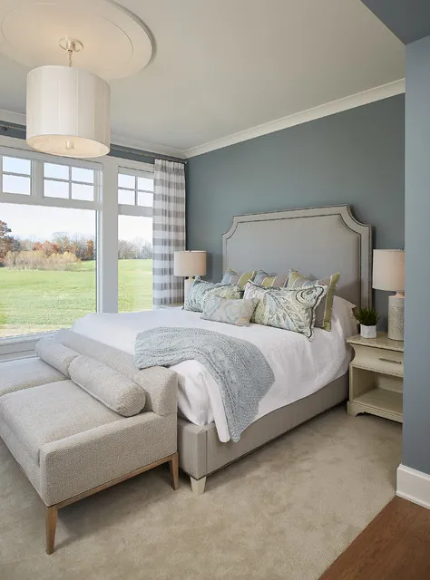 A light upholstered bed sits in a gray room beside broad windows.