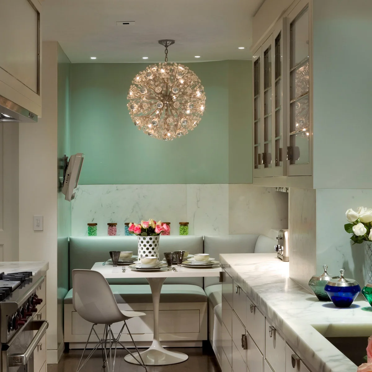 Pale galley kitchen ending in a compact banquette with mint wall and round pedestal table