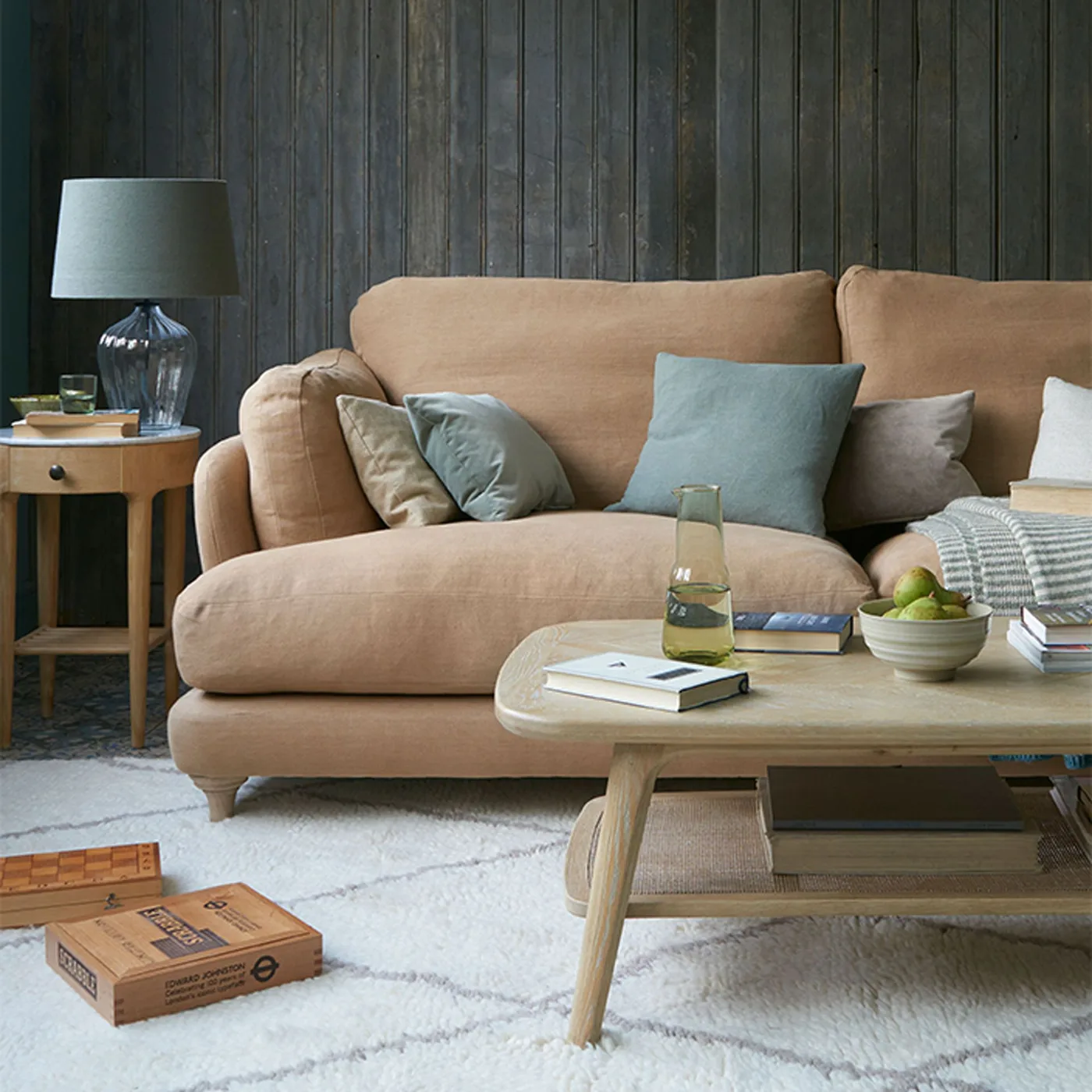 Tan couch with muted green and neutral pillows against a dark paneled wall.