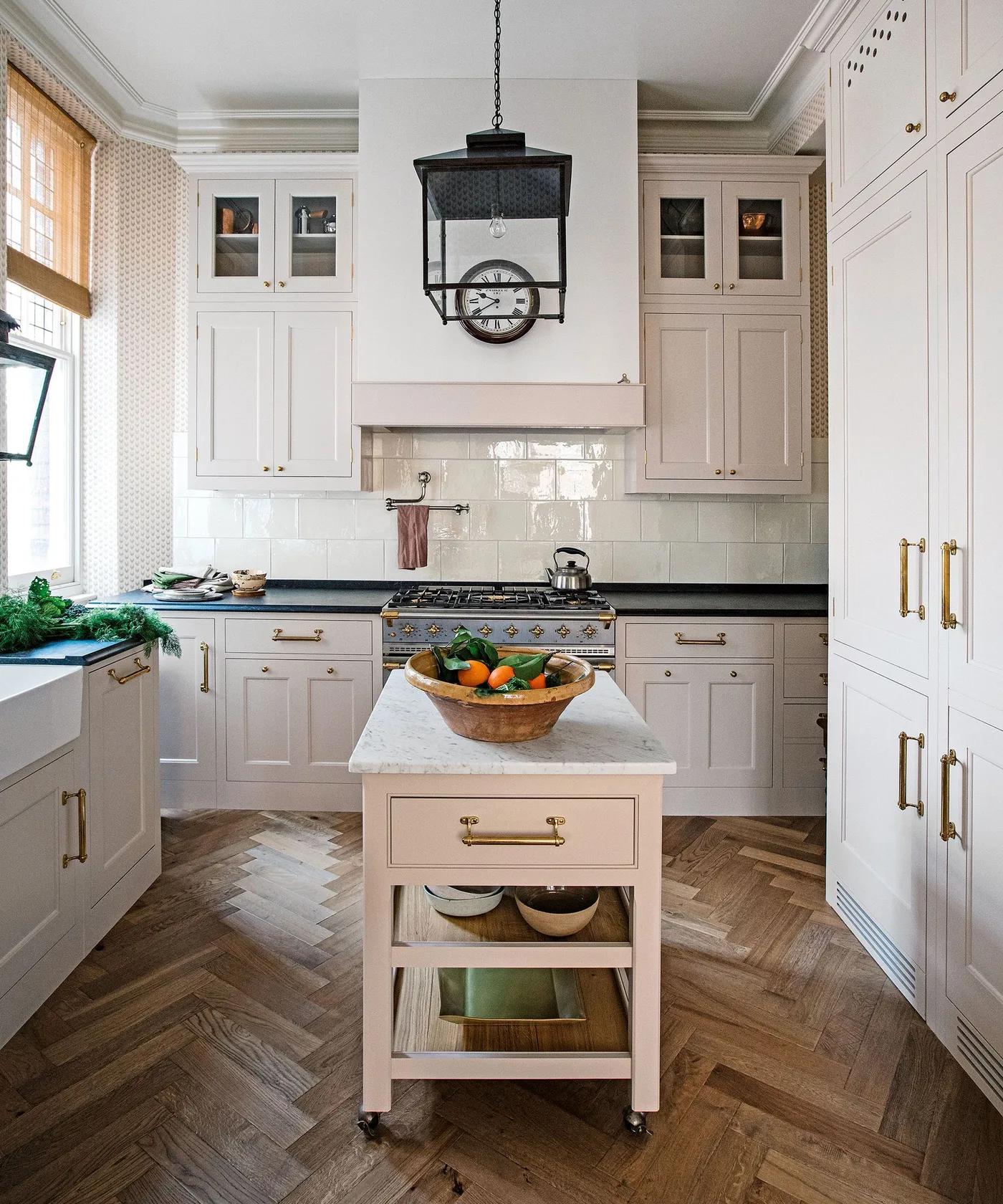 Pale paneled kitchen with a dark range cooker, black lantern pendant and a small wheeled island with open shelves.