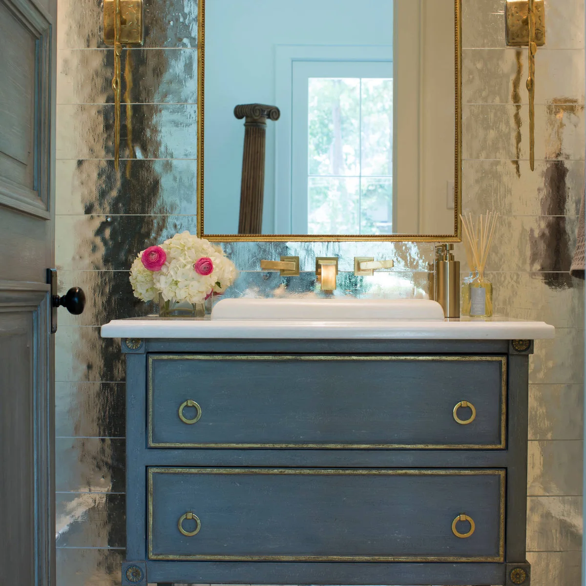 Gold-colored framed mirror on a mottled reflective wall above a blue vanity
