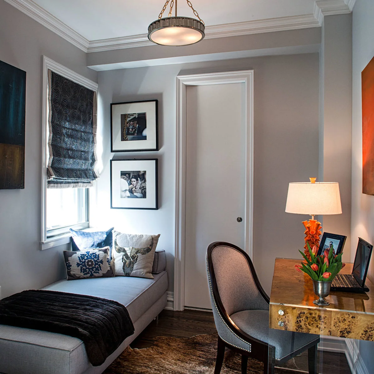 Small gray office with a wood desk, upholstered chair, orange lamp and pale daybed beneath the window