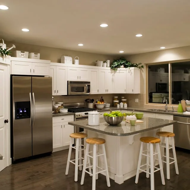 White baskets and small pale containers above a white kitchen cabinet run with greenery concentrated near the right corner.
