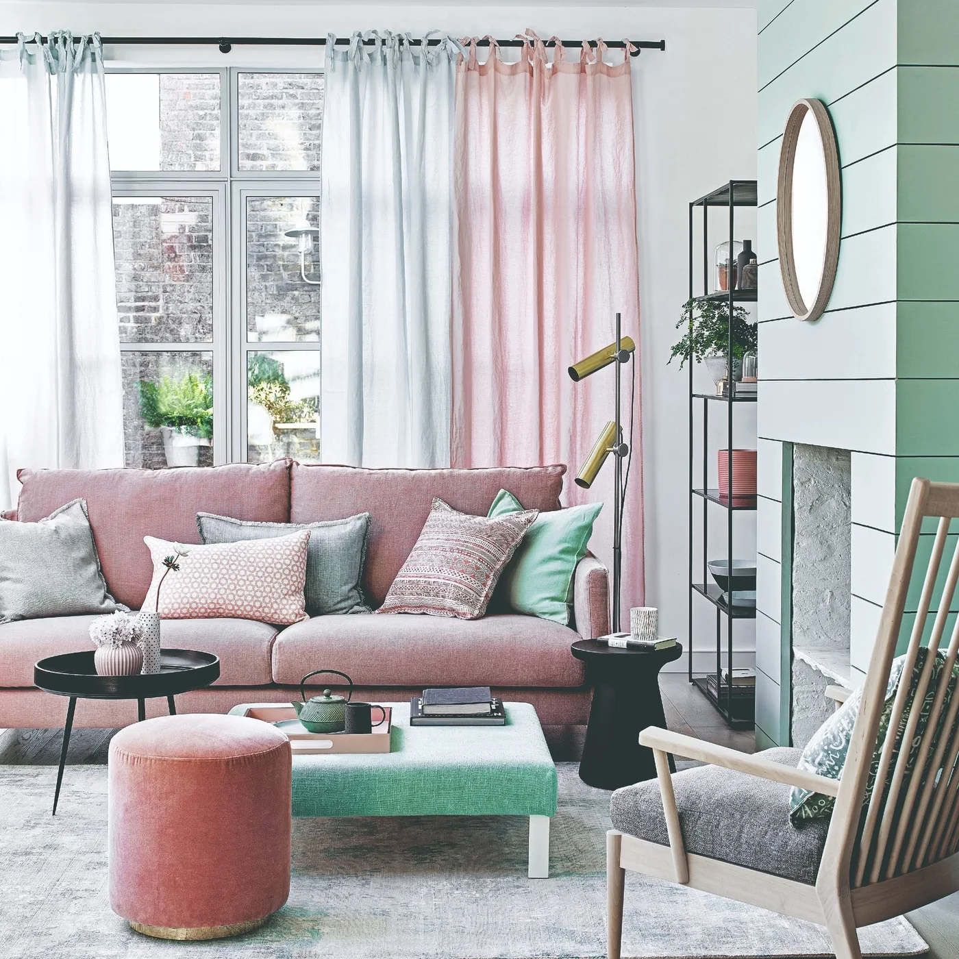 A pink sofa sits beneath pale mint and pink curtain panels beside a mint-painted chimney breast and small upholstered tables.