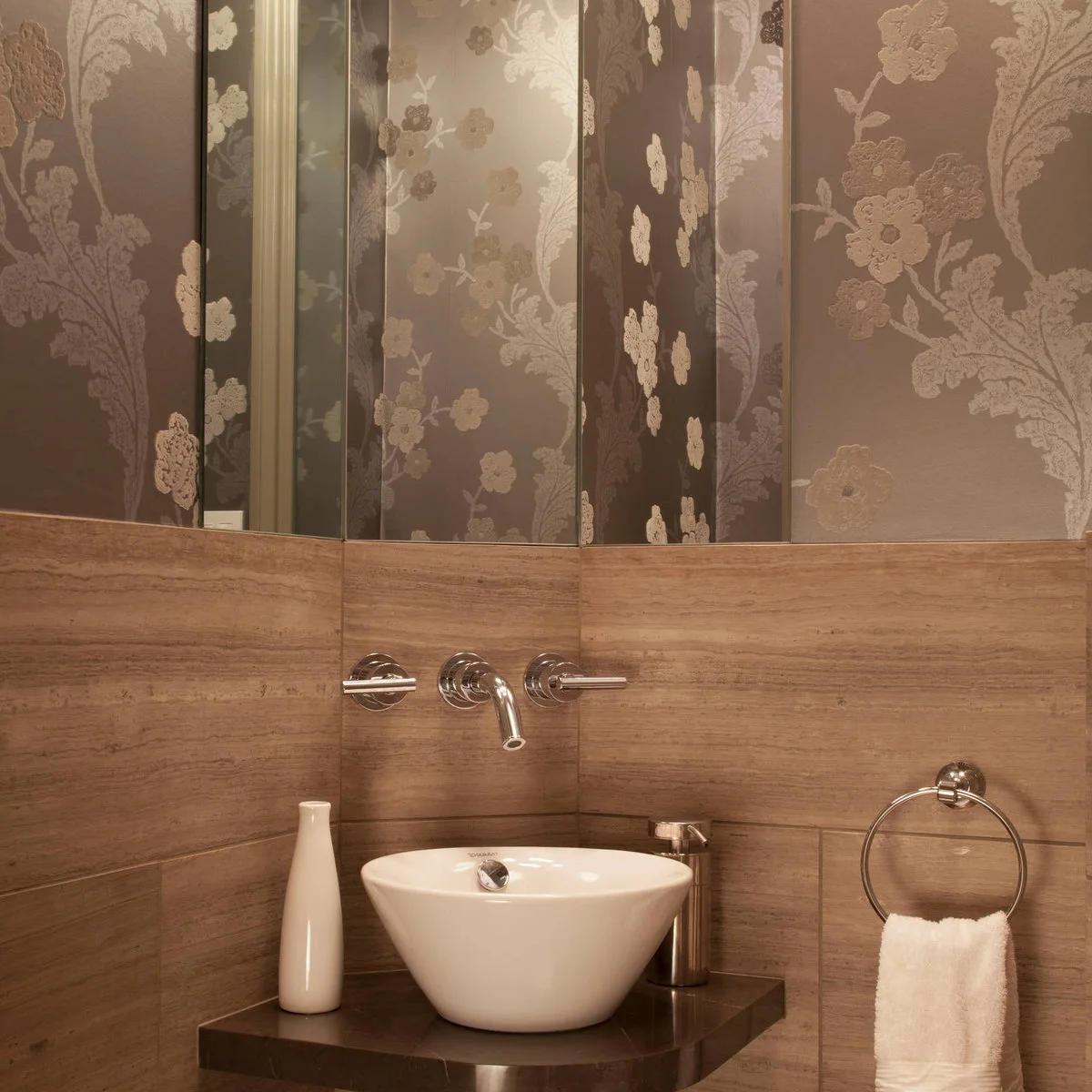 A chrome towel ring hangs beside a white vessel sink on a small dark counter beneath a wall-mounted faucet.