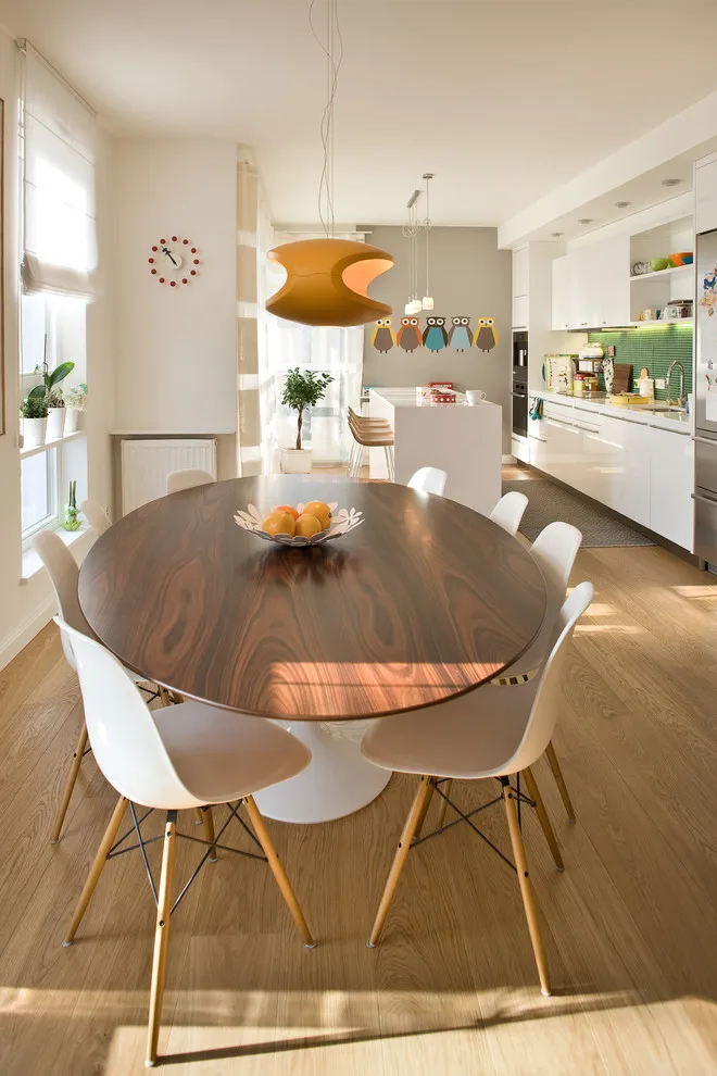 An oval timber table sits beside white chairs in a long apartment kitchen-dining area