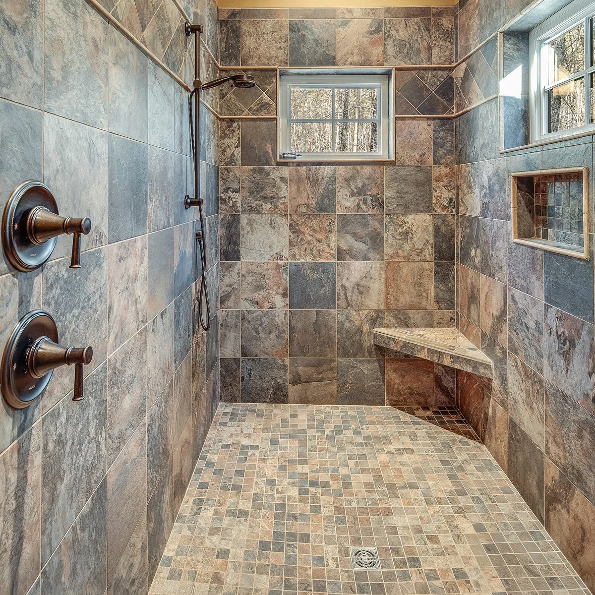 A shower with mottled gray, brown and warm rust-colored square tiles, two windows, a recessed niche and a triangular corner seat.