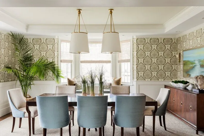 Blue upholstered chairs around a dark dining table with two shaded pendants and a long wooden sideboard.