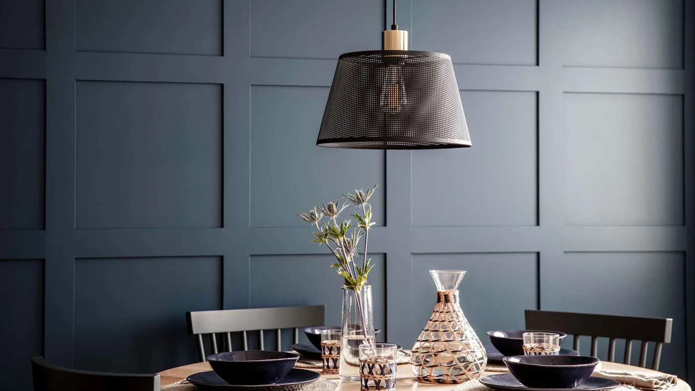 Black mesh pendant above a dining table with dark chairs against blue-gray paneled walls