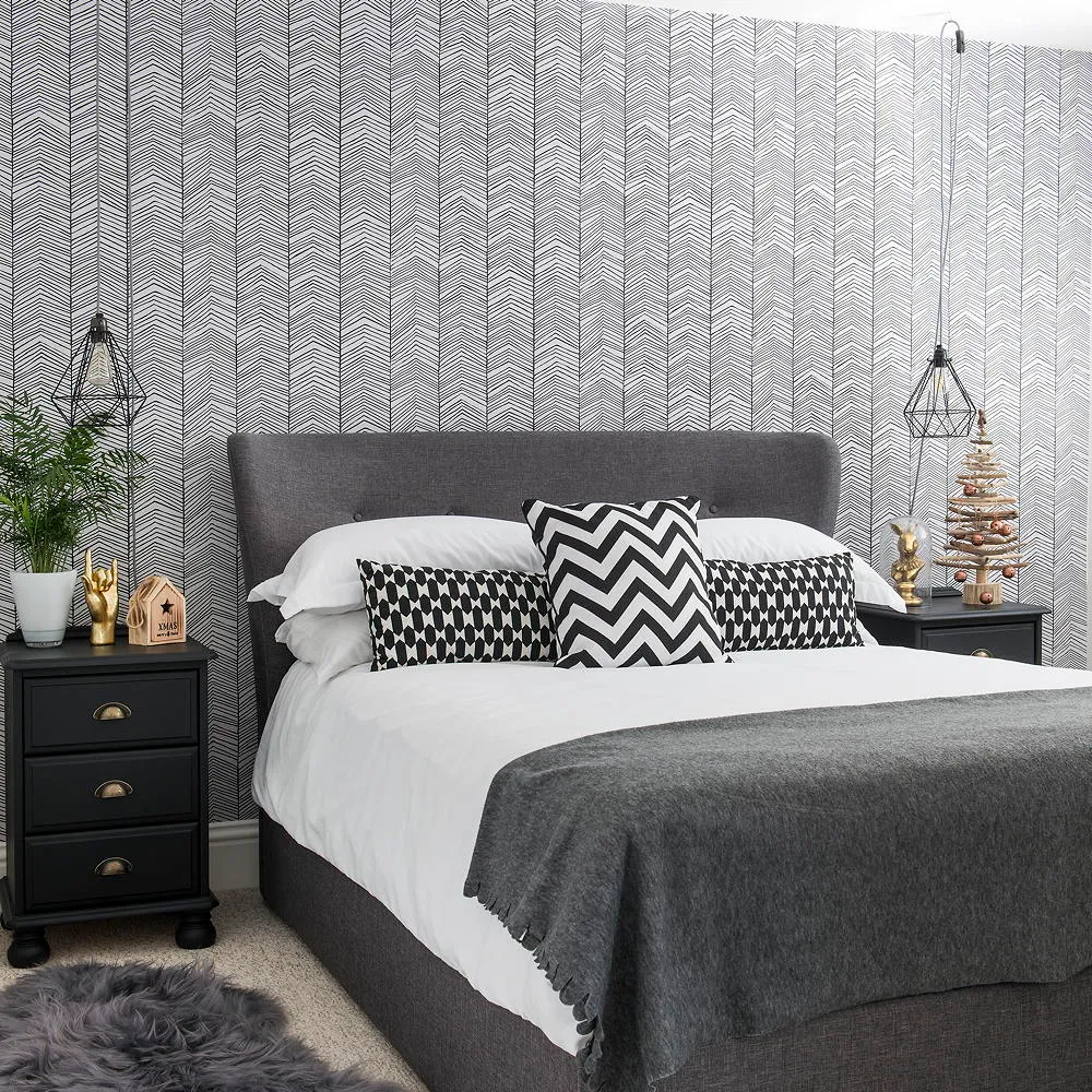 A small black-and-white wall pattern sits behind gray bedding and zigzag cushions