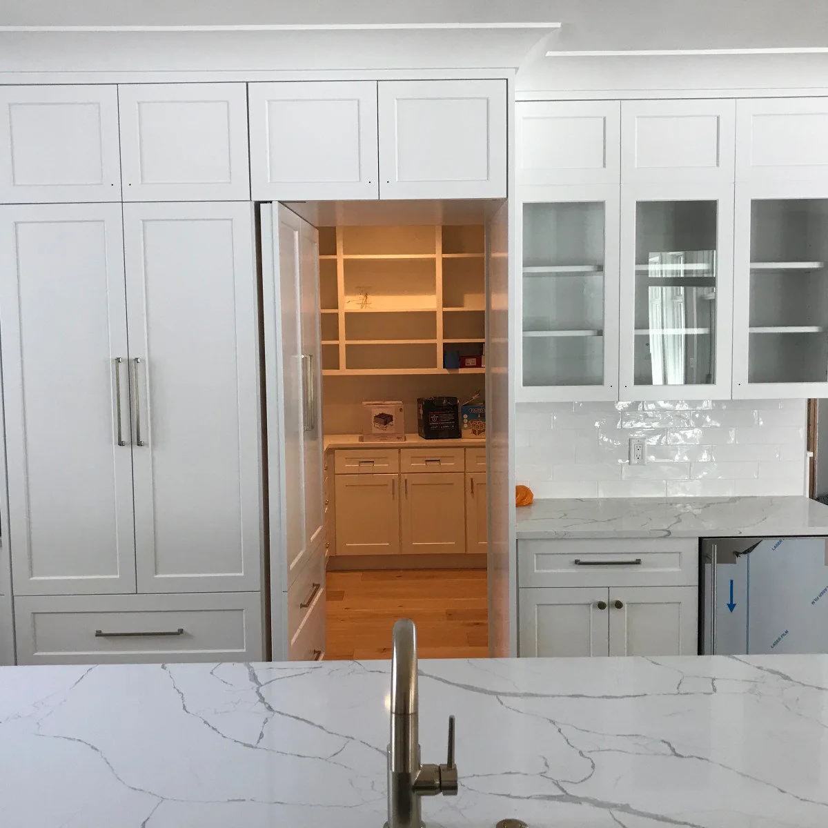 An open white cabinet-style doorway reveals pantry shelves and a lower counter beside tall white kitchen cabinetry.