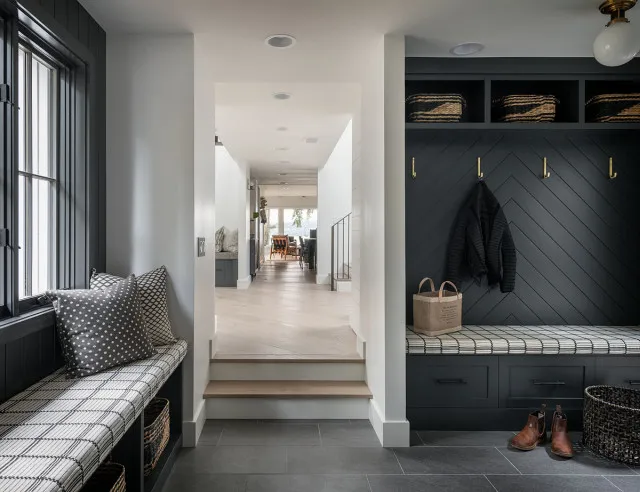 Dark coat-storage recess and long window bench with checked cushions above dark tiled flooring