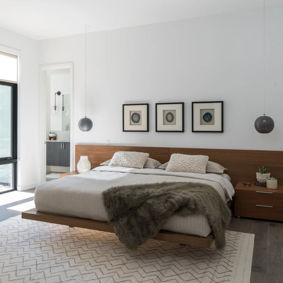 A cream rug with thin gray zigzag lines extends beneath a wood platform bed in a white bedroom.