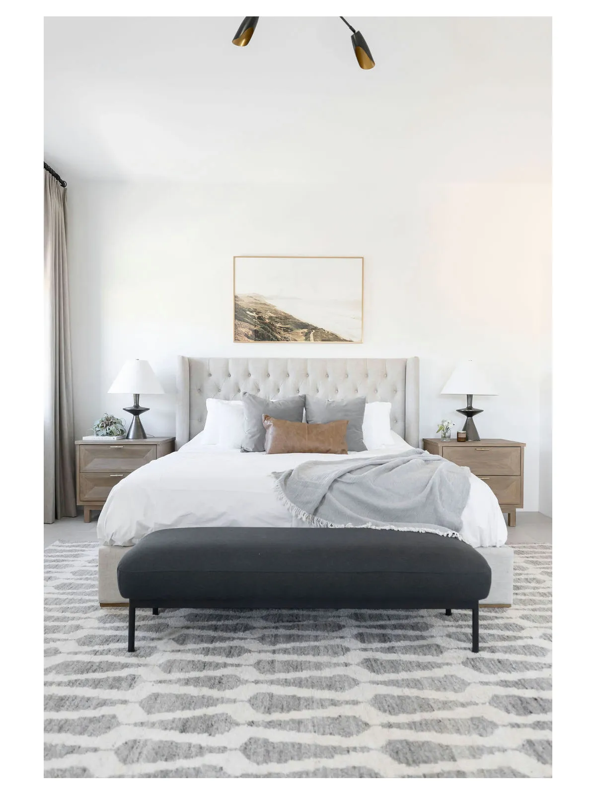 A pale bed sits behind a dark upholstered bench on a subtly patterned rug.