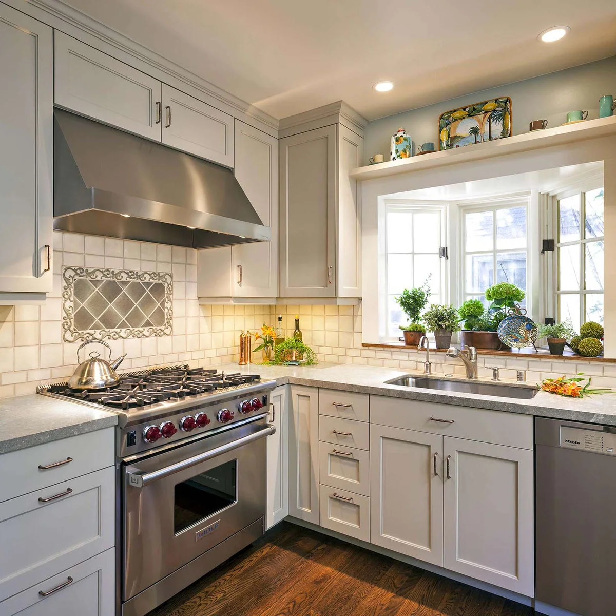 A shallow kitchen bay window above a sink with several potted plants and a high shelf of colorful ceramics.