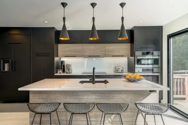 A broad black cabinet wall stands behind a pale island under three dark-and-gold pendants.