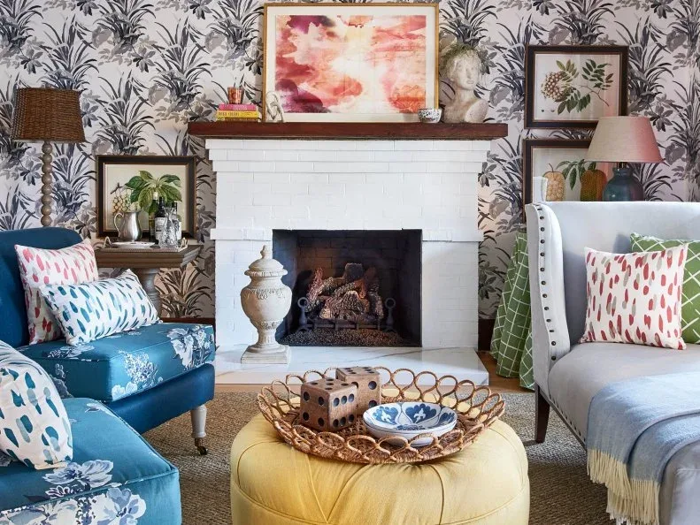 White brick fireplace with wood mantel, pink and orange artwork, books, decorative head and leafy wallpaper