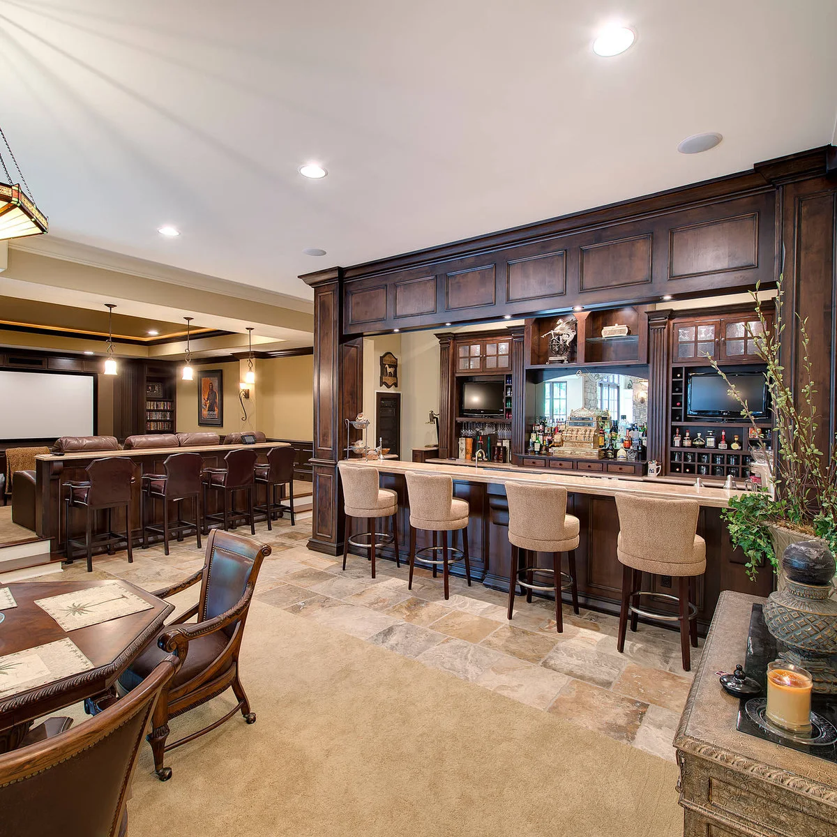 Large basement with traditional wood-colored bar, pale stools and separate cinema seating beyond