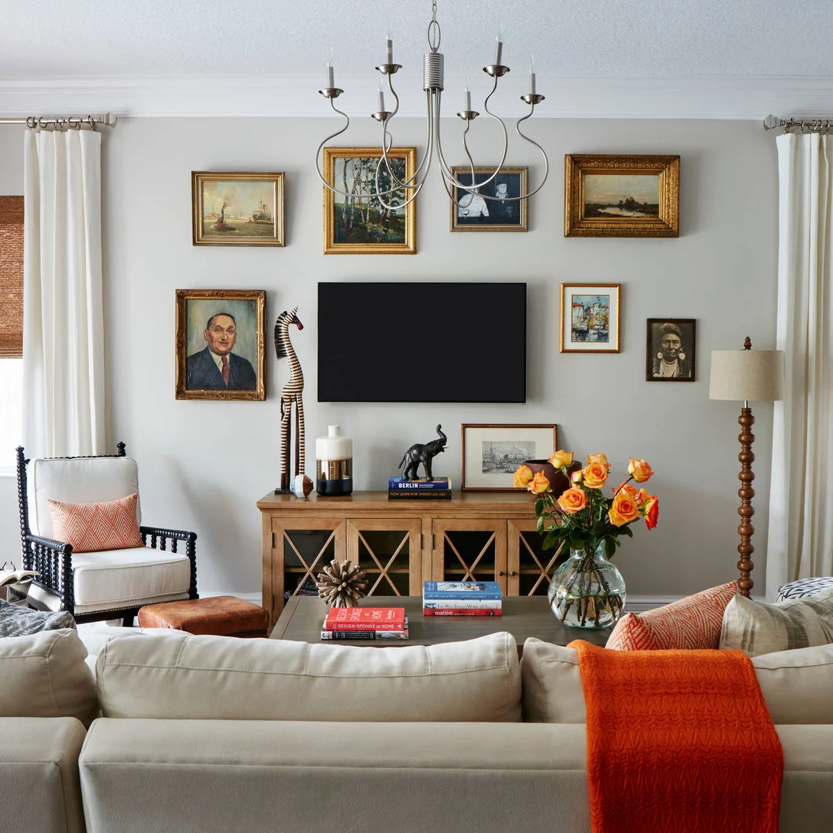 Gold and dark-framed portraits and landscapes arranged above and beside a wall-mounted television over a wood cabinet.