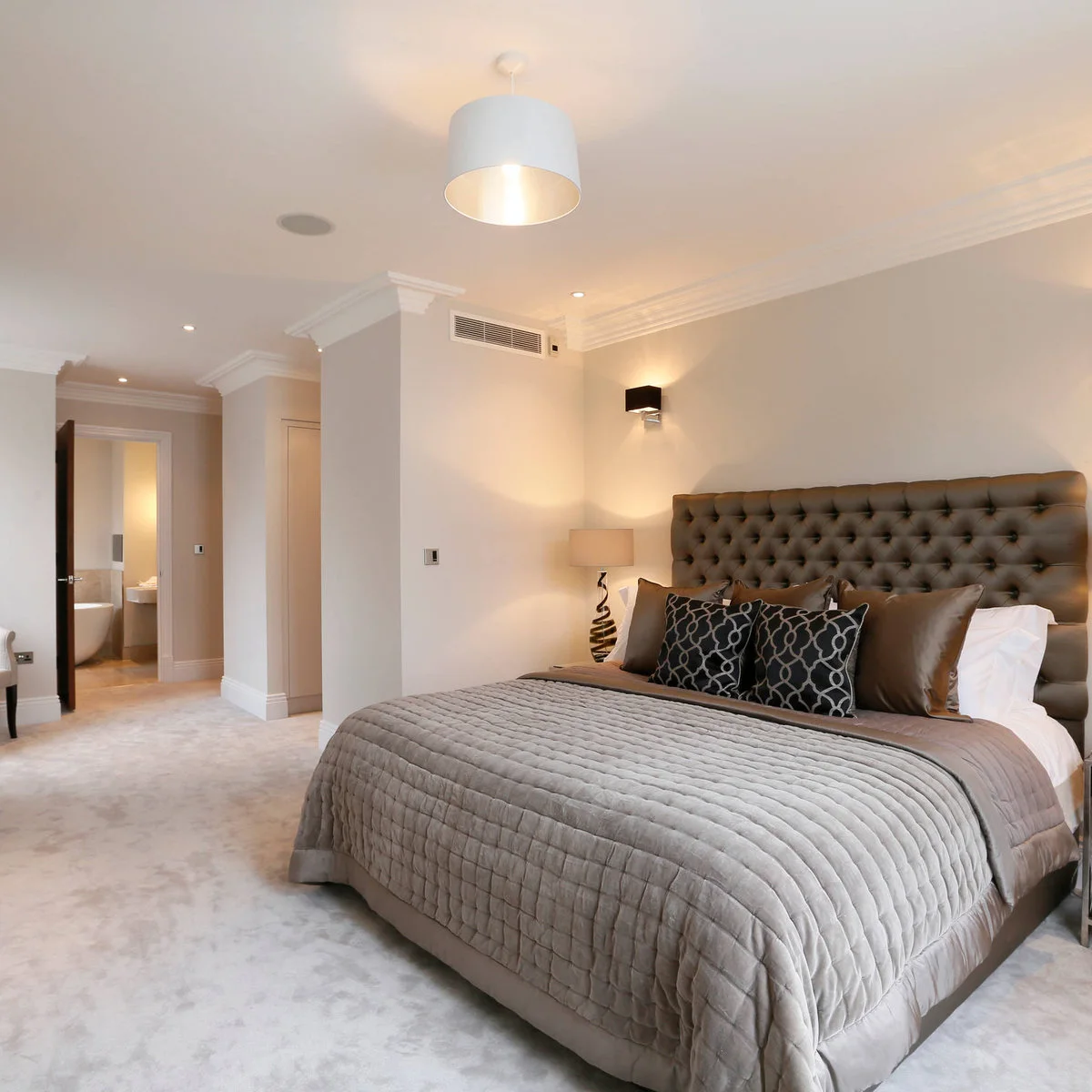Brown tufted headboard and cushions with a gray quilt in a cream bedroom.