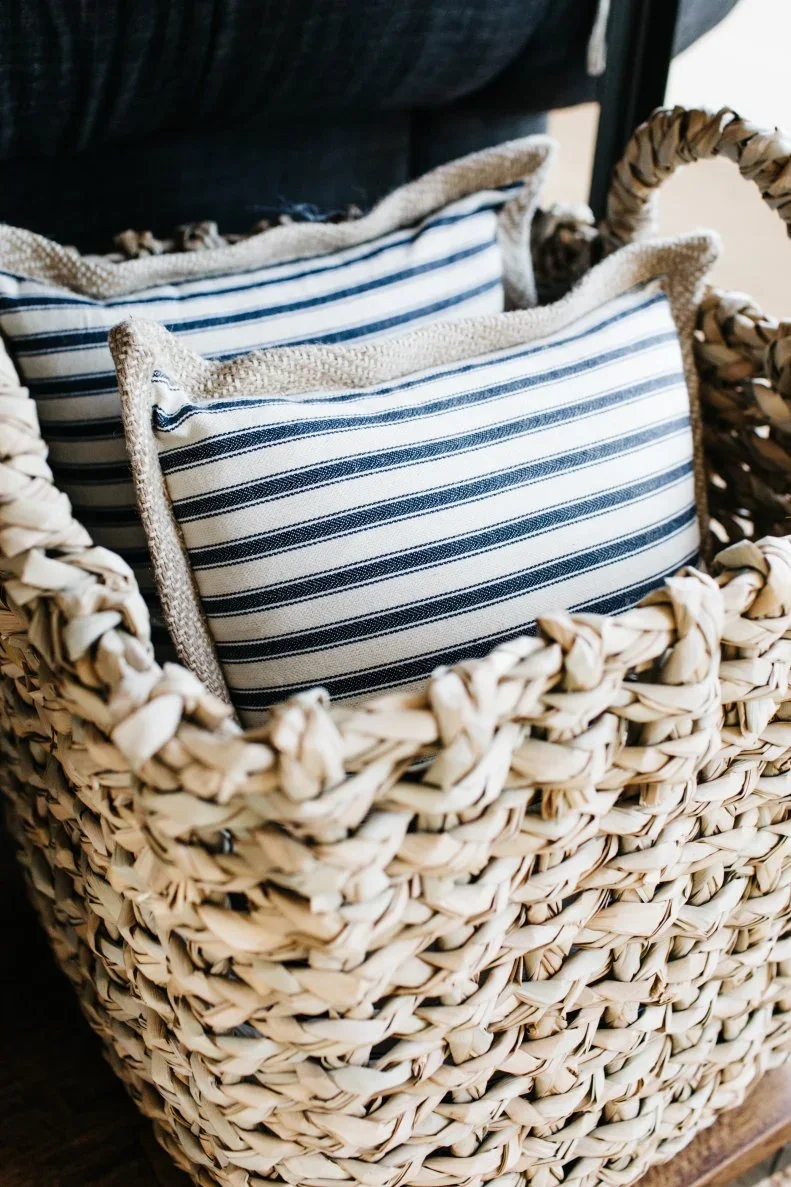 Blue-and-white striped cushions with textured edging sit upright in a handled woven basket.