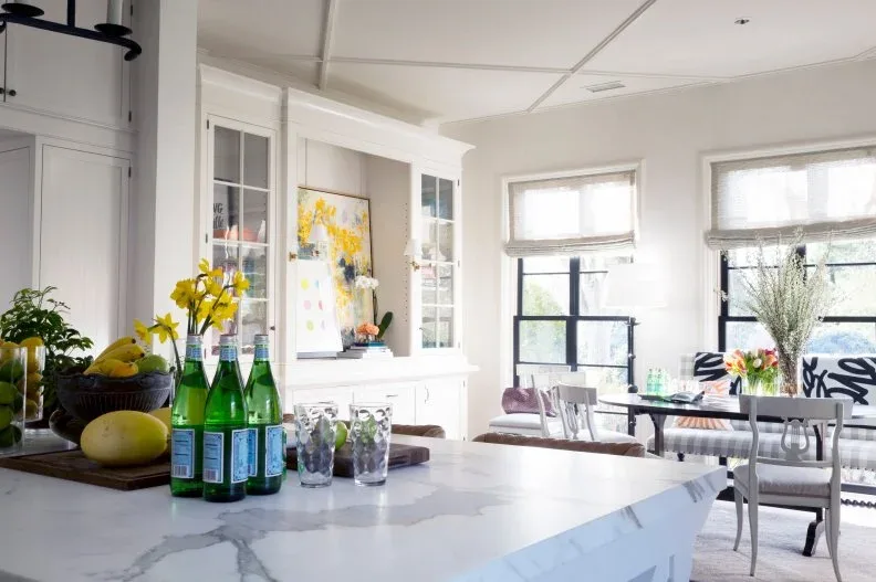 Pale folded shades on black-framed windows behind a breakfast nook with patterned seating