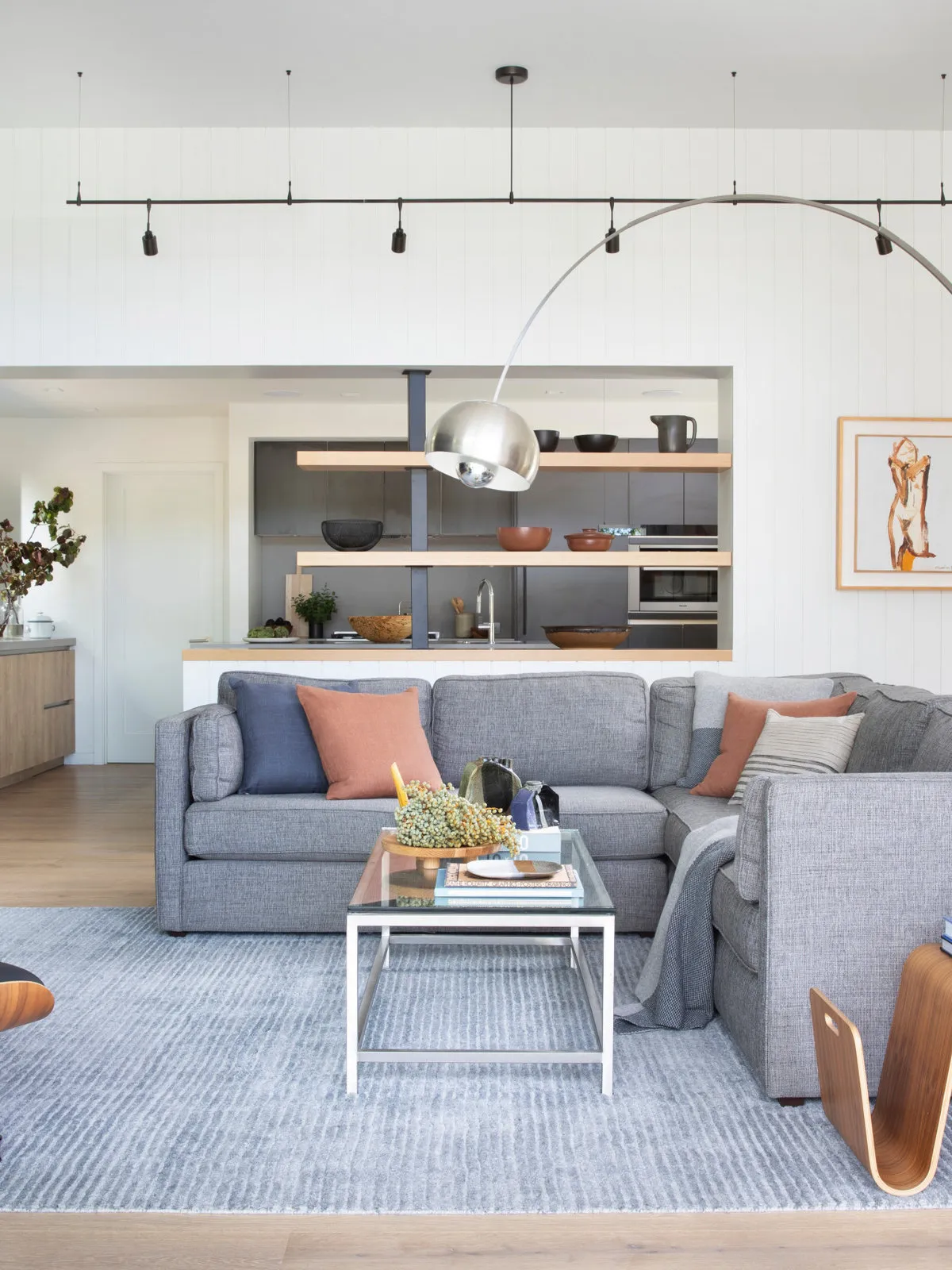 A gray sofa sits below light walls with soft warm-colored cushions and a pale table.