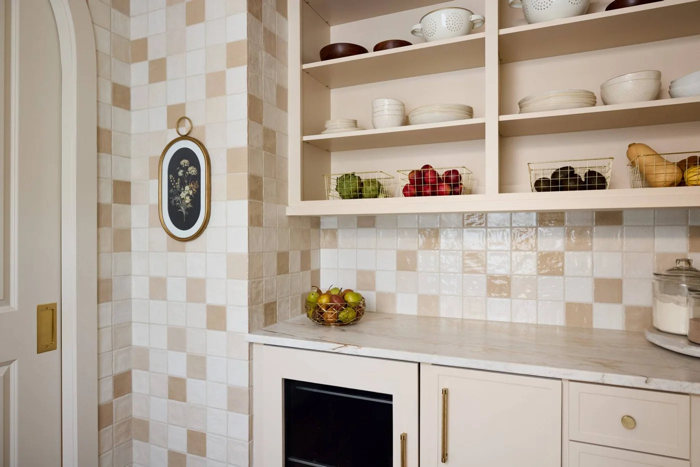 White and cream square kitchen tiles wrap a corner beside open shelving, a pale counter and a built-in microwave.