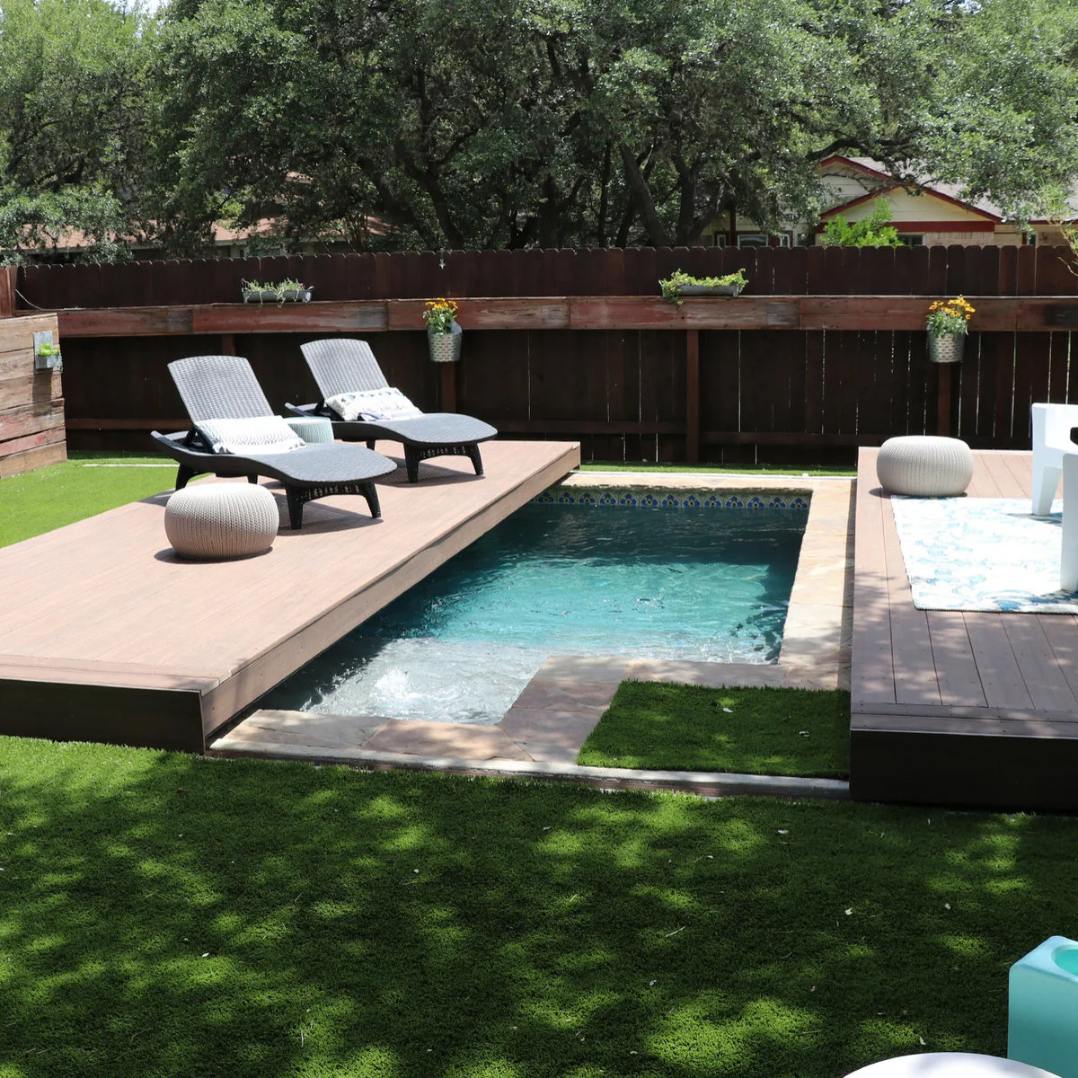 A small rectangular pool is partly revealed beside a deck carrying two loungers, with wood fencing and planted boxes behind it.