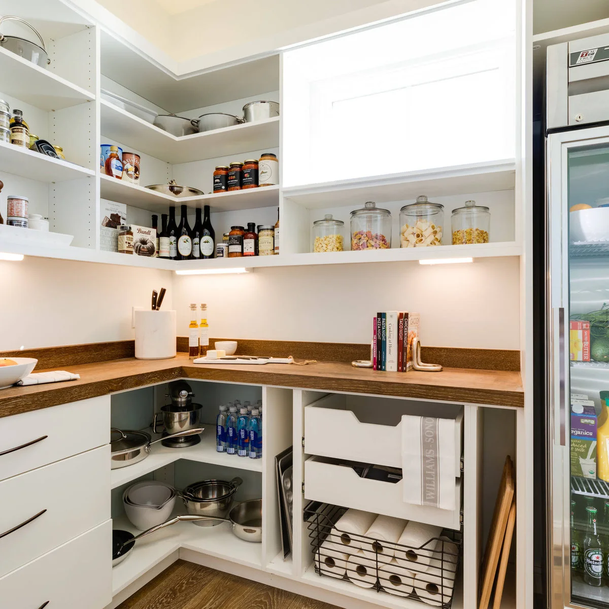 White pantry with lower open shelves for pans and a mixer beneath a wood counter