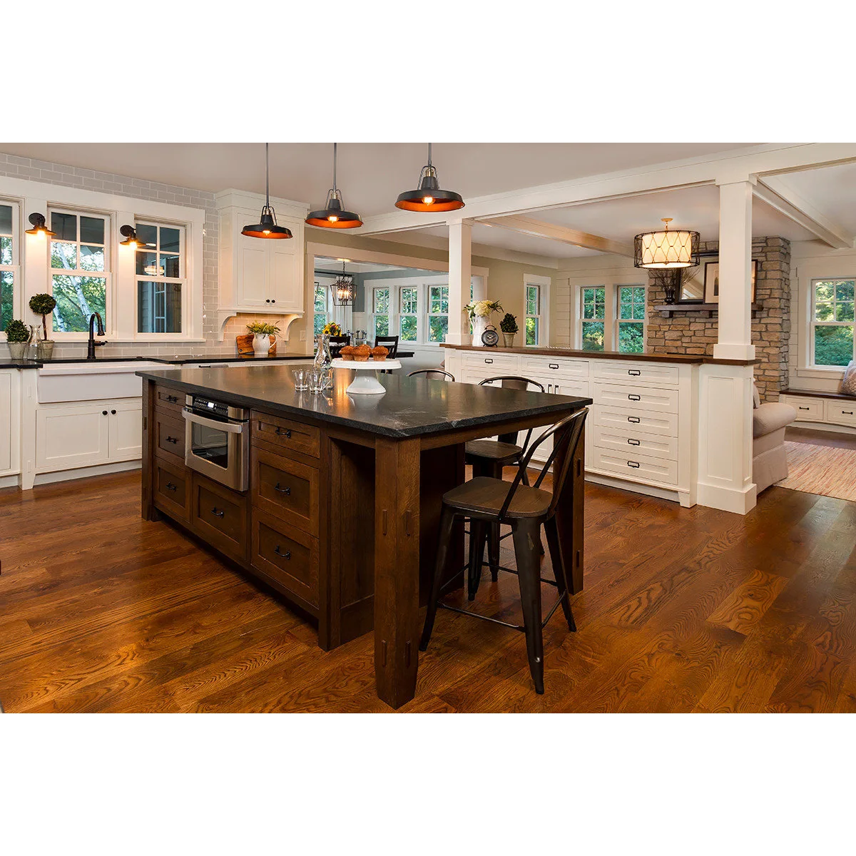 White drawers and two white posts divide a farmhouse kitchen from a sitting room with a stone fireplace.
