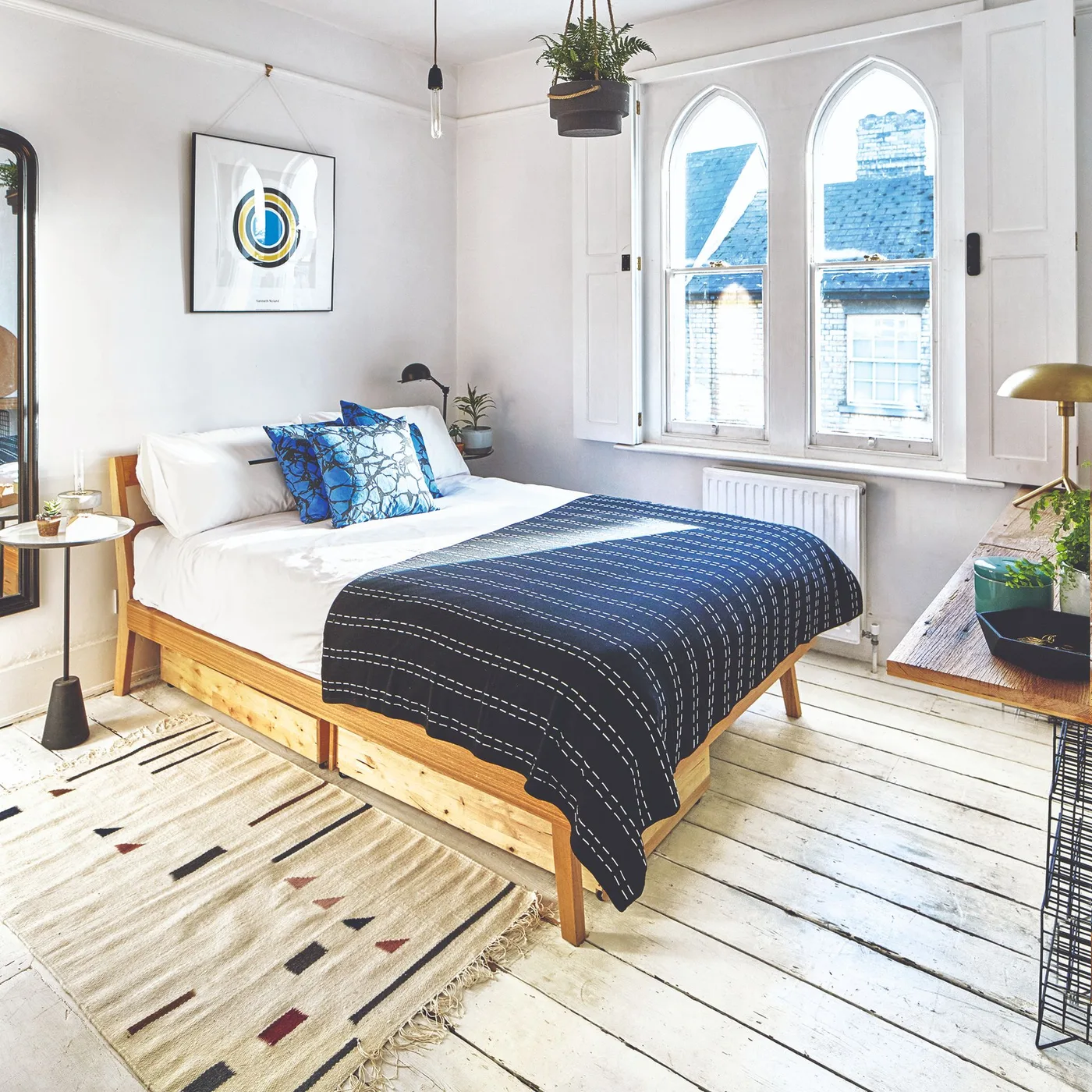 White bedroom with arched windows, a wooden bed, dark blue patterned bedding and cushions, and a light woven rug.