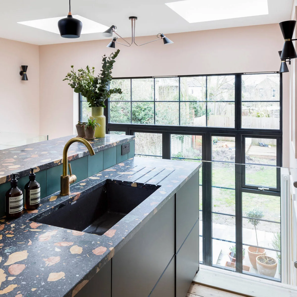 Terraced-house kitchen with patterned counters, a gold-colored faucet and tall rear glazing beside descending steps