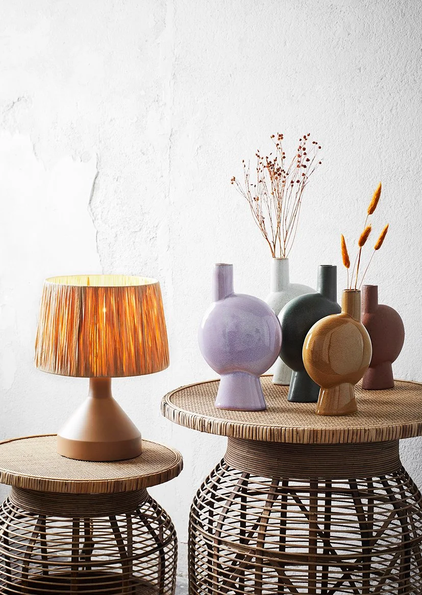 Five rounded vases in pale purple, gray, charcoal, ochre and dusty pink sit together, with dry stems in only two vessels.