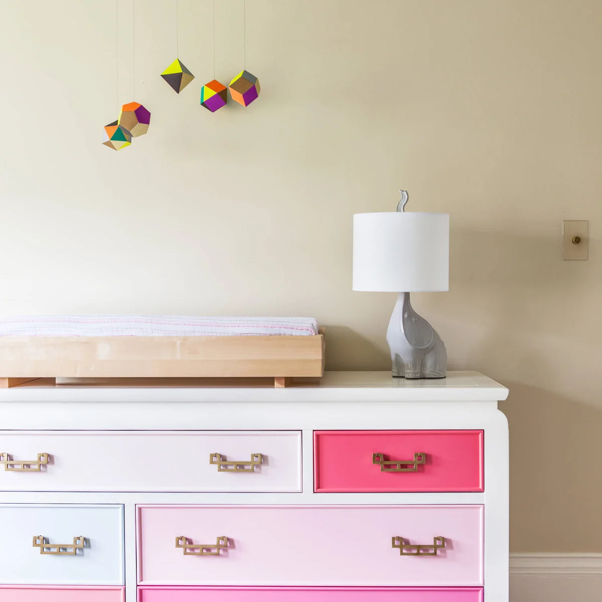 Nursery dresser with pink and pale blue drawer fronts, gold-colored handles and an elephant lamp