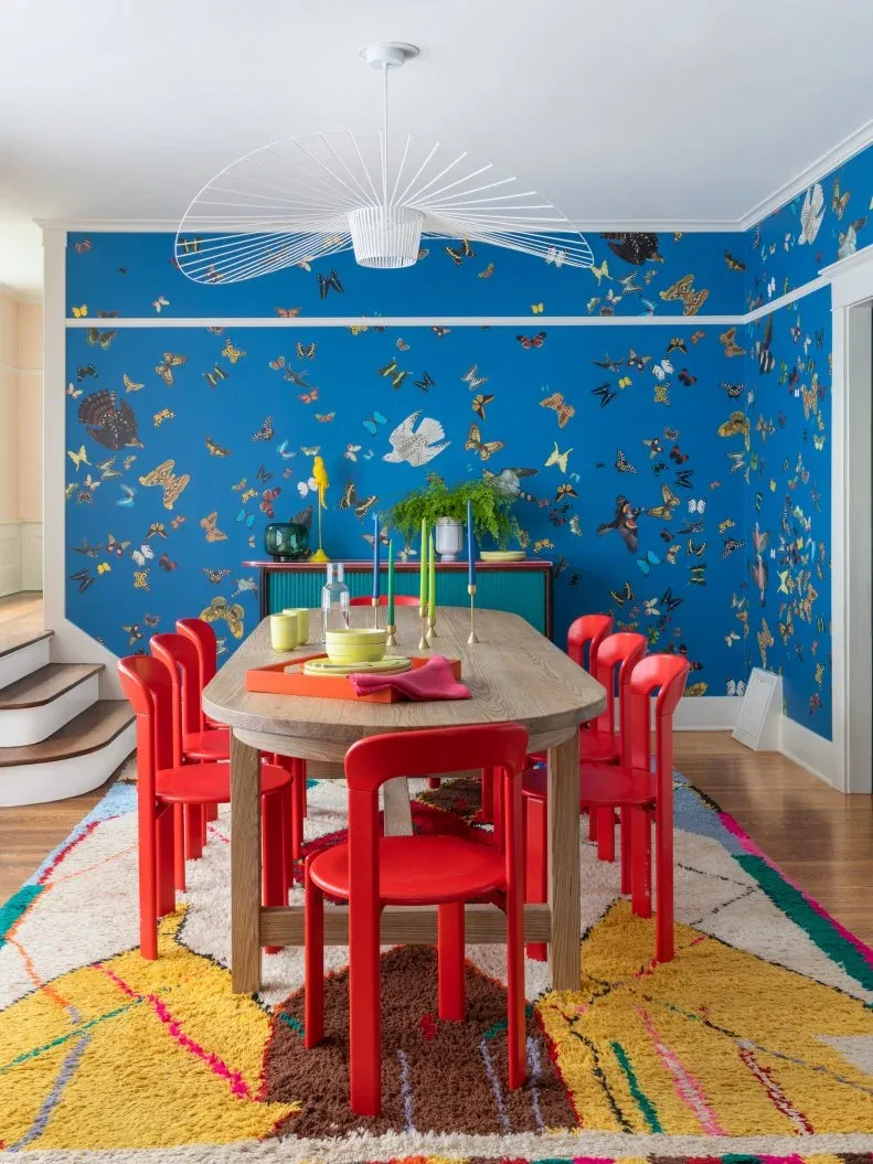 Teal sideboard with a contrasting red top behind an oval wood table and red chairs against bright blue wallpaper