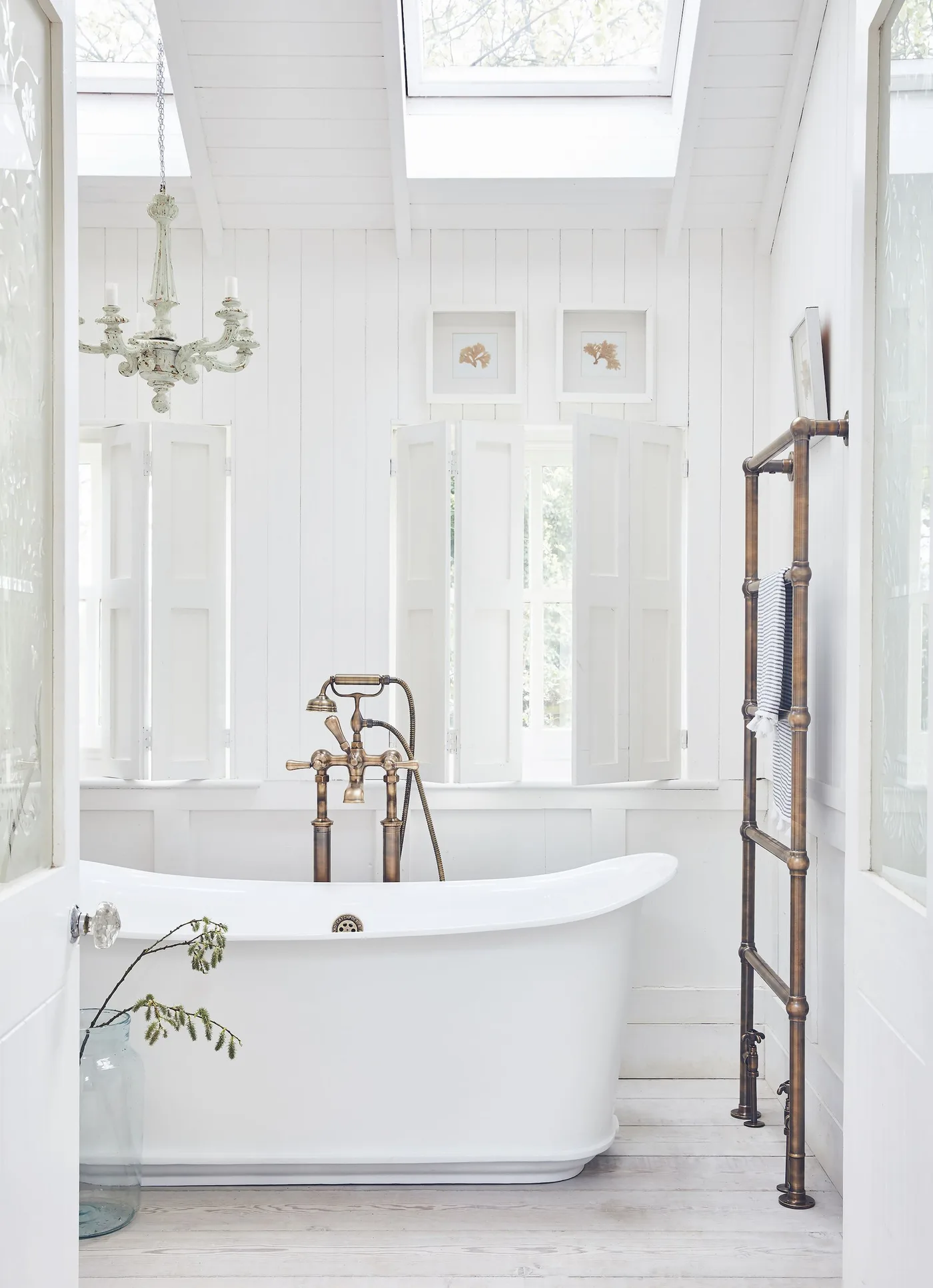 Bright bathroom with a white freestanding tub, white wall paneling, a sloped ceiling and a tall metal towel rail.