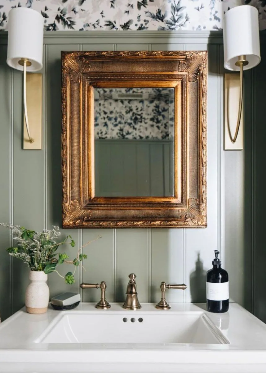 Sage paneled wash area with ornate warm-toned mirror, white sink and bird-pattern upper wall