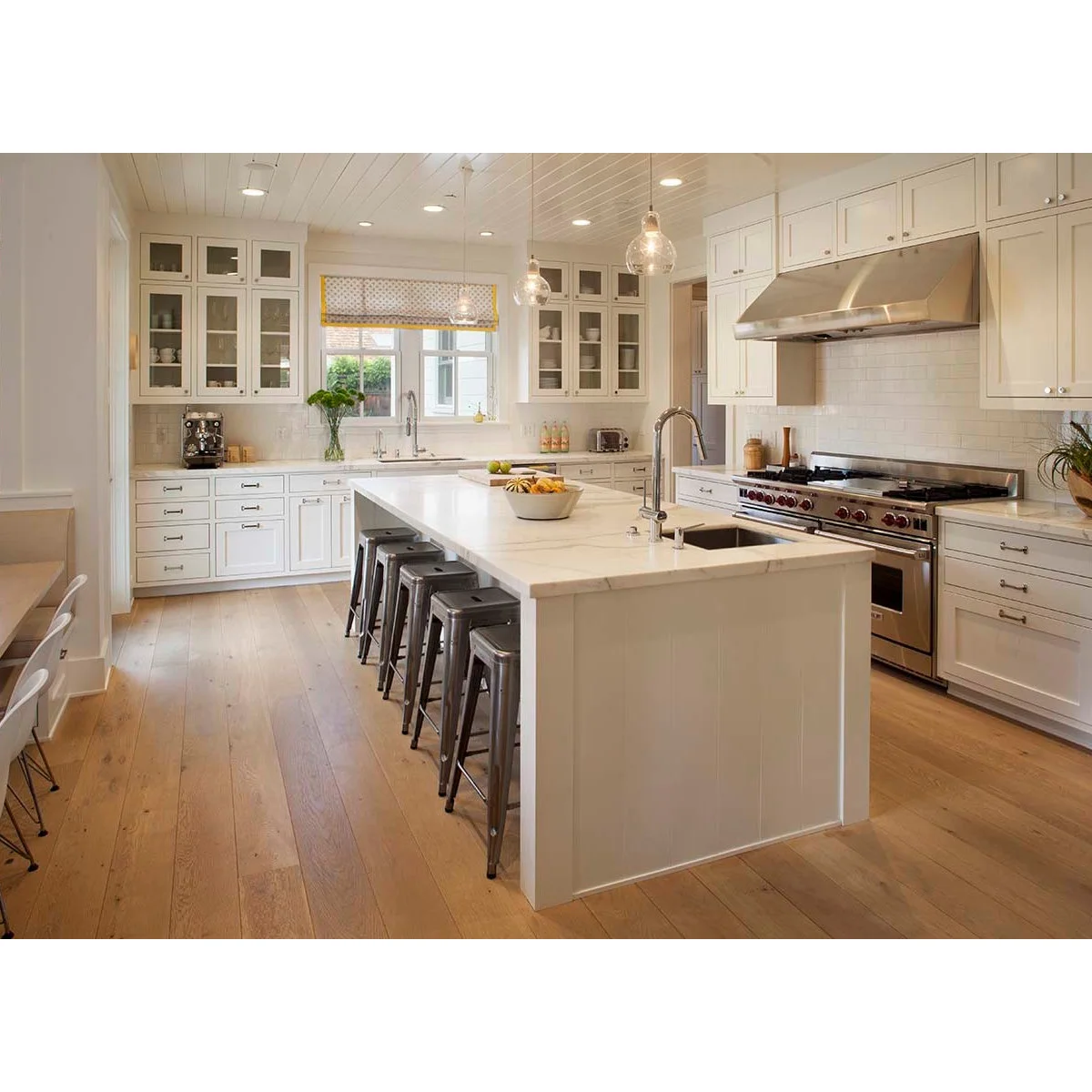 A patterned blind with a yellow edge above a sink window between white glass-fronted kitchen cabinets.