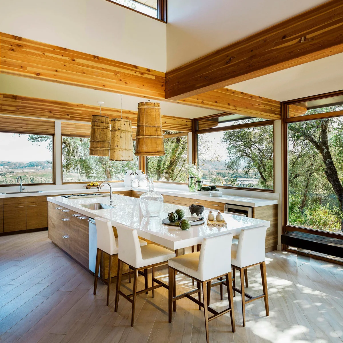 Wood kitchen island with a sink at one end and light chairs around the other