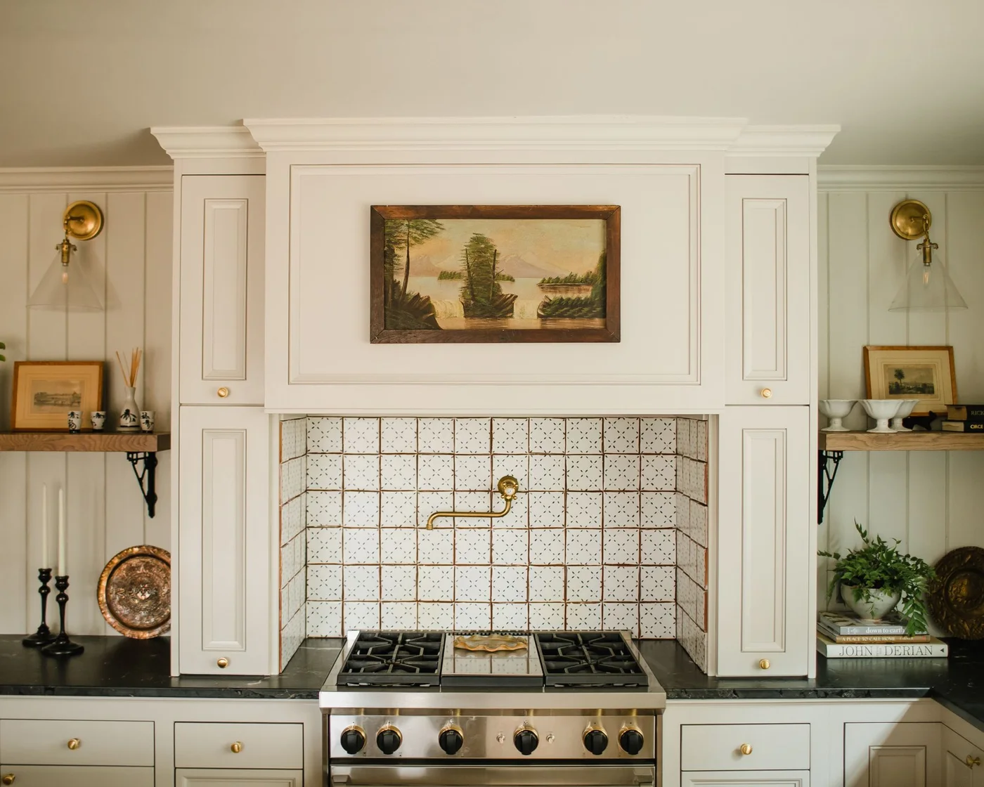 Creamy cupboards frame a range niche with small patterned tiles, a dark counter and warm metal knobs.