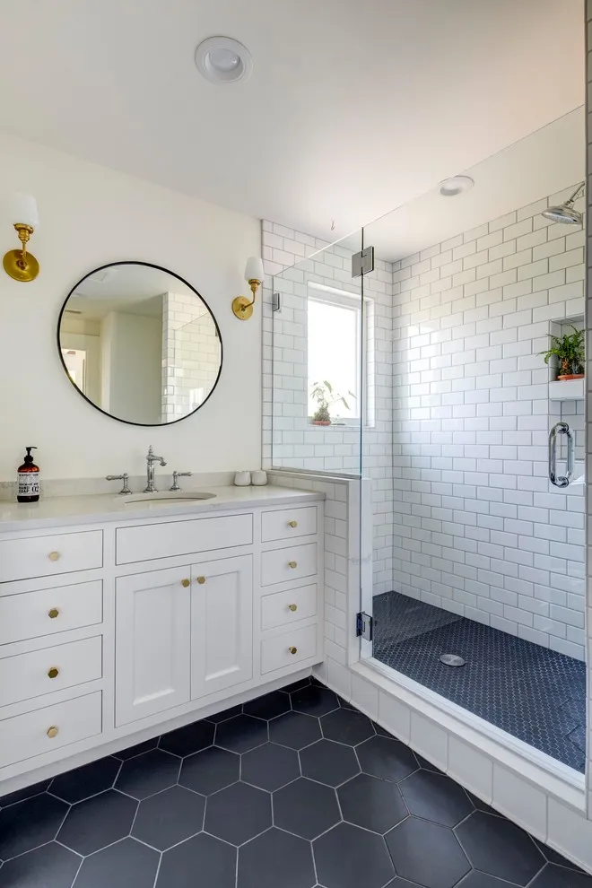 Dark hexagonal tiles sit beneath a white vanity beside a glass shower